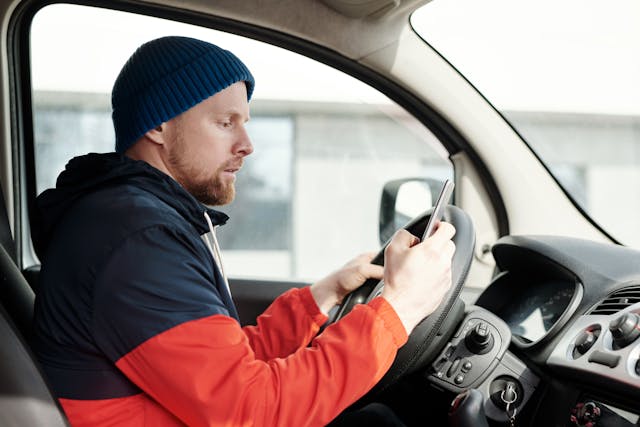 Man sitting in vehicle using smartphone to help with work.