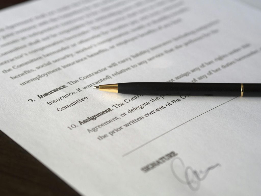 Close-up view of a contract document with sections on insurance and assignment highlighted, with a black pen resting on top, symbolizing business agreements and legal documentation.